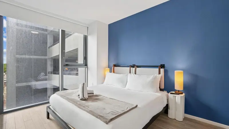 Chambre lumineuse avec un grand lit et une baie vitrée.