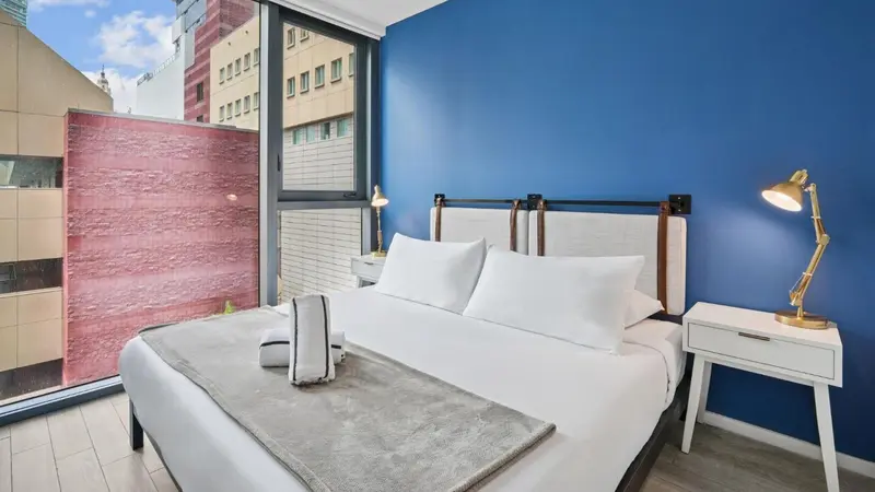 Une chambre lumineuse avec un grand lit recouvert d'une courtepointe grise et de coussins blancs.