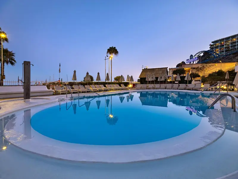 Piscine extérieure avec transats et végétation au crépuscule.