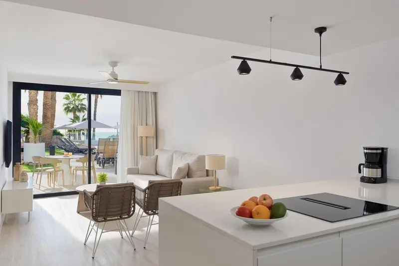 Espace de vie lumineux avec canapé, table basse et cuisine équipée donnant sur une terrasse.