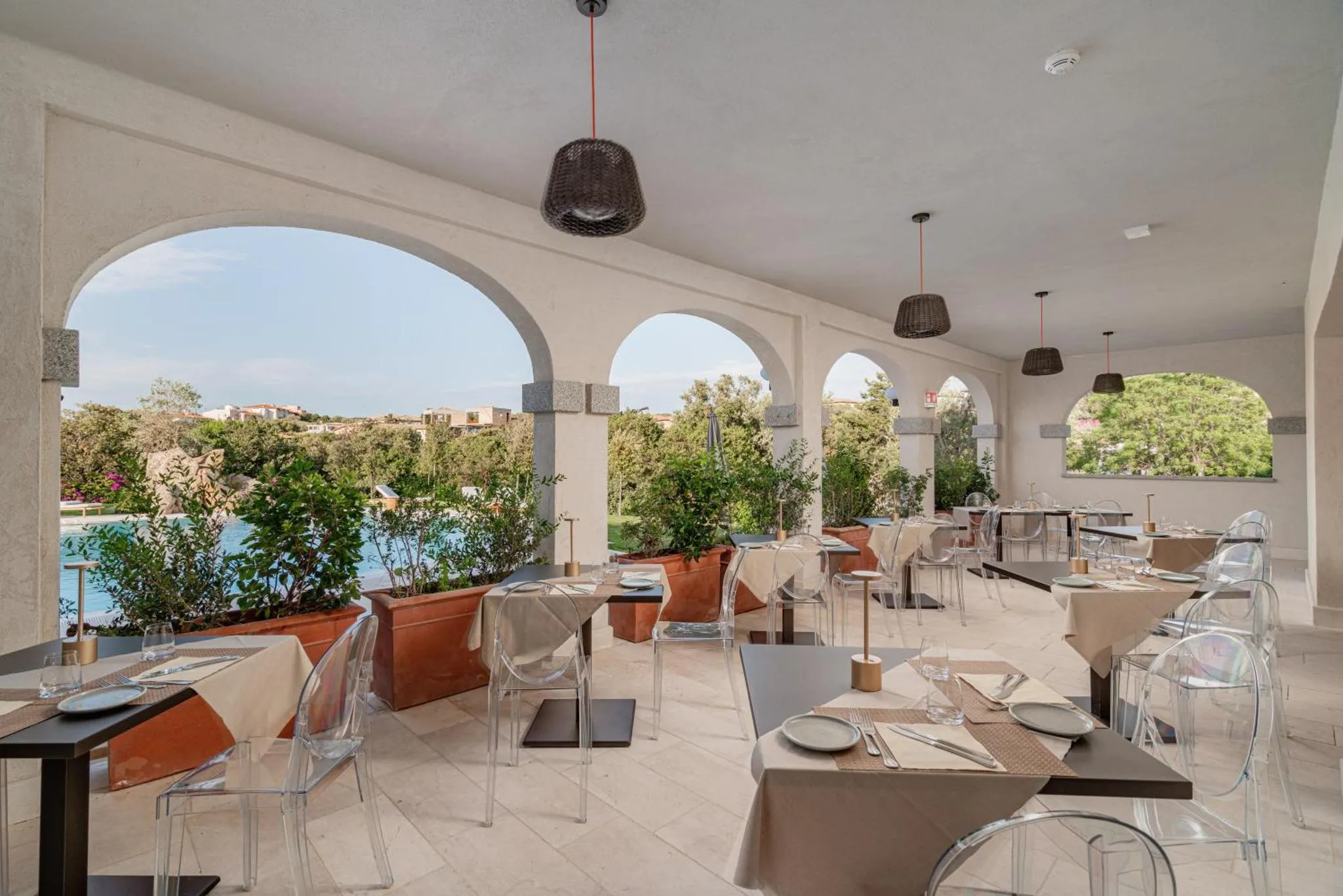 Terrasse ombragée avec tables et chaises face à un paysage verdoyant.