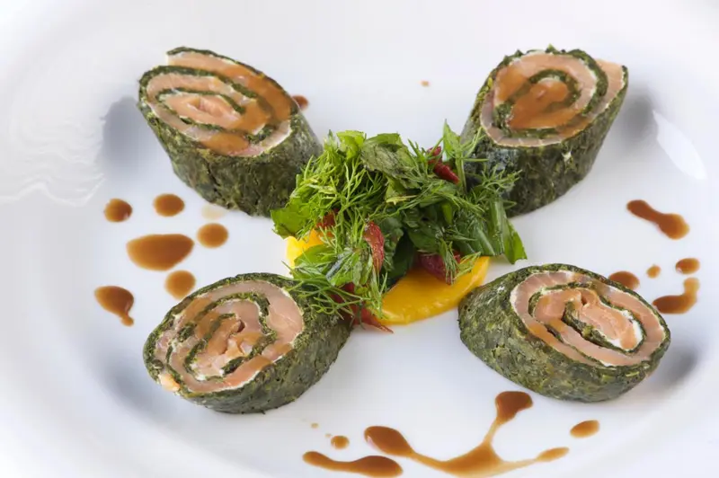 Assiette de rouleaux de saumon et d'algues, décorée de sauce et de verdure.