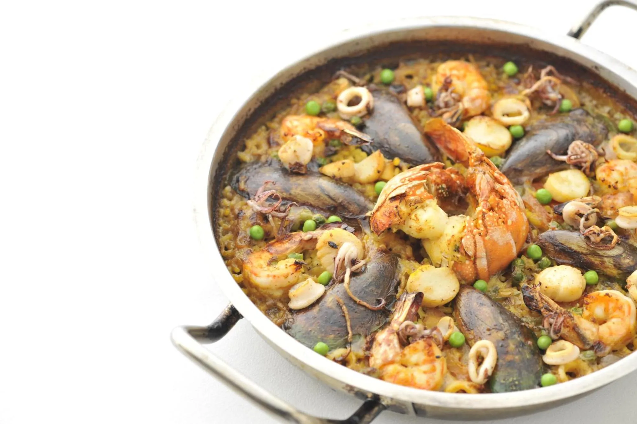 Une grande poêle en métal présente une paella généreusement garnie de fruits de mer et de légumes.