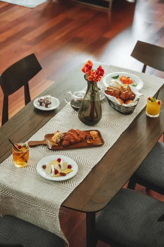 Une table en bois est dressée pour un repas avec des viennoiseries et des boissons.