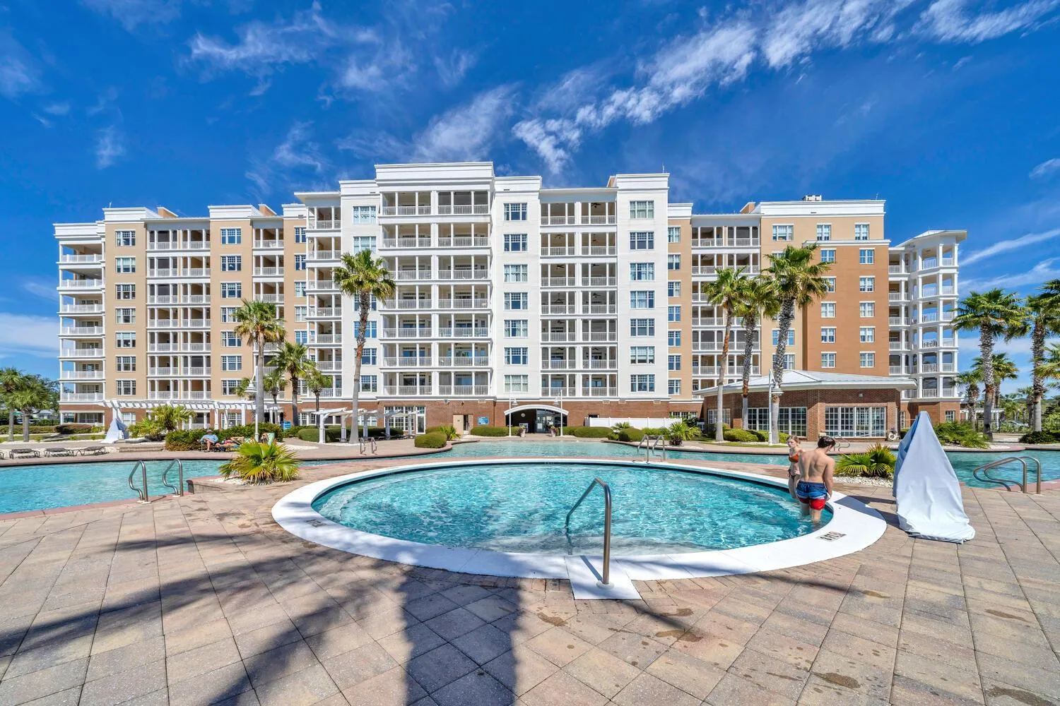 Bâtiment beige et blanc avec des balcons, surplombant une piscine et une zone de détente.