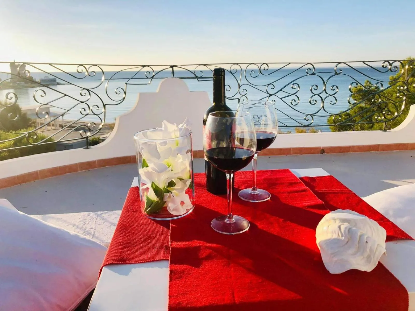 Une table dressée avec une bouteille de vin et des verres sur une terrasse ensoleillée avec vue sur la mer.