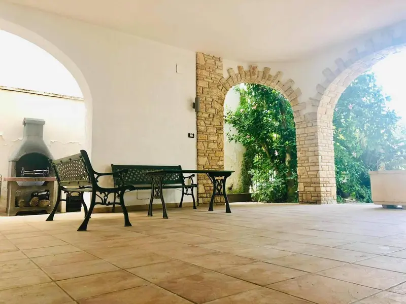 Espace extérieur ombragé avec mobilier de jardin et barbecue en pierre.