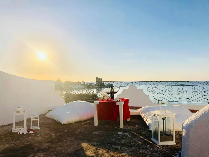 Terrasse aménagée avec table et assises blanches face à la mer au lever du soleil.