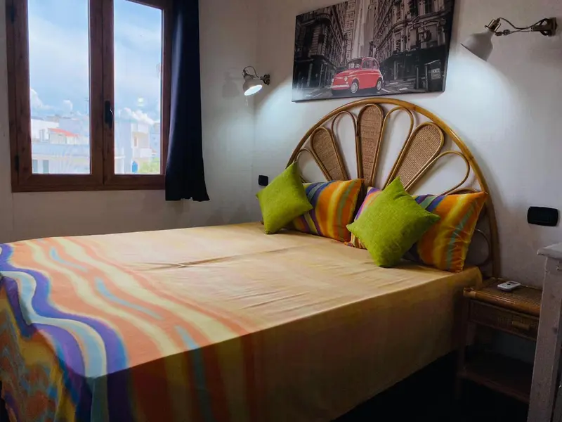 Une chambre lumineuse avec un lit recouvert d'une courtepointe colorée et un tableau décoratif.