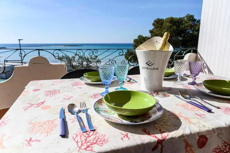 Une table dressée avec de la vaisselle et une bouteille de champagne sur une terrasse ensoleillée.