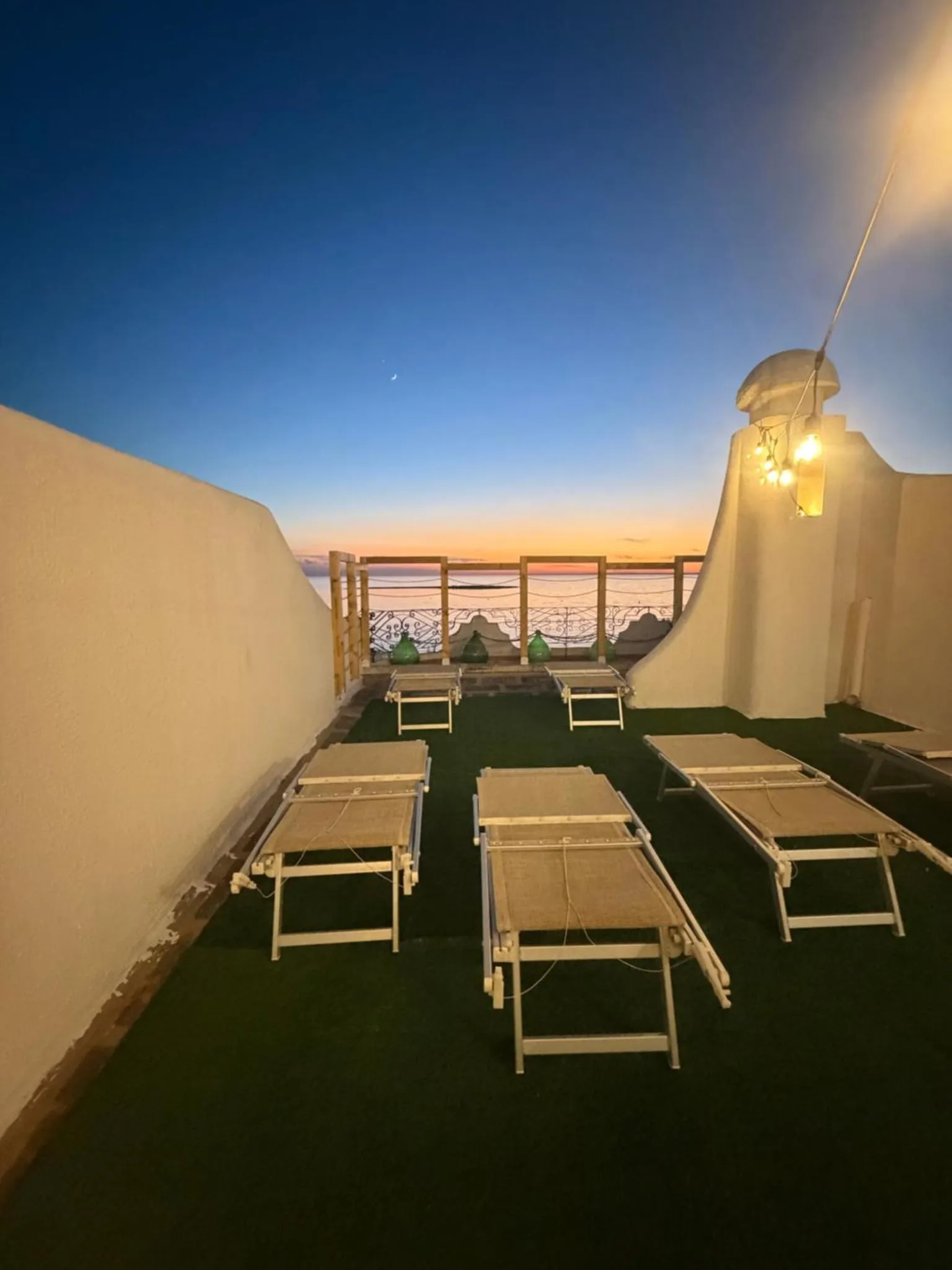Terrasse avec transats et vue sur la mer au crépuscule.