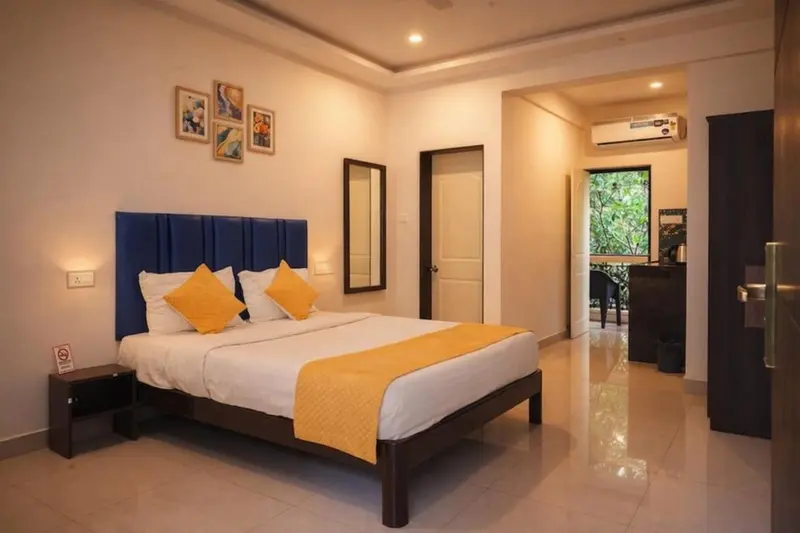 Chambre lumineuse avec un grand lit recouvert d'une courtepointe jaune et de coussins.