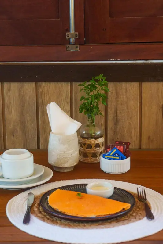 Une table est dressée avec un petit-déjeuner composé d'une omelette, d'une tasse de café et de couverts.