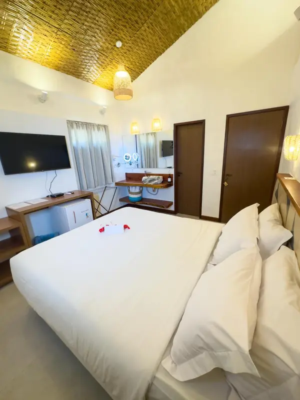 Une chambre lumineuse avec un lit recouvert de blanc et un téléviseur mural.