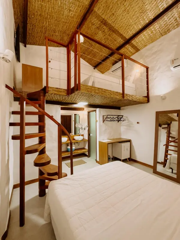 Une chambre avec un lit blanc et un escalier en colimaçon menant à une mezzanine.
