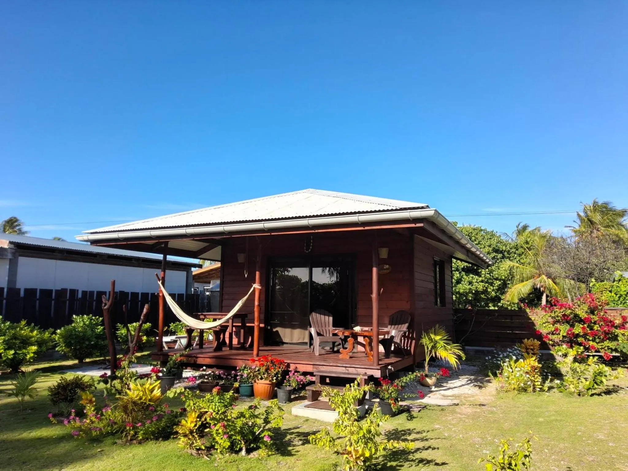 Une petite maison en bois rouge avec une terrasse ombragée et un hamac.