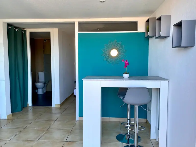 Une table avec deux tabourets se trouve devant un mur turquoise décoré d'un soleil.