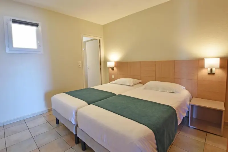 Une chambre lumineuse avec deux lits simples et une décoration sobre.