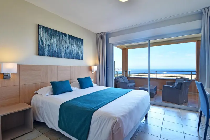 Une chambre lumineuse avec un grand lit et un accès à une terrasse offrant une vue sur la mer.
