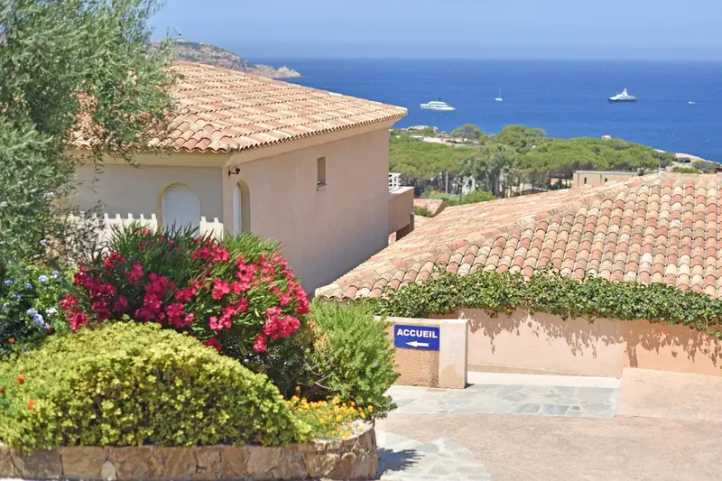 Bâtiment aux tuiles rouges et végétation fleurie surplombant la mer.