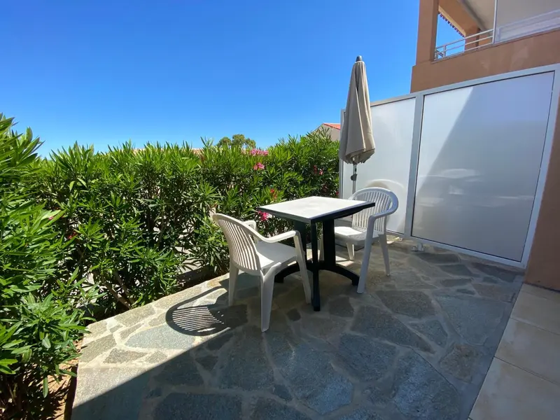 Une table et des chaises en plastique sur une terrasse pavée ensoleillée.