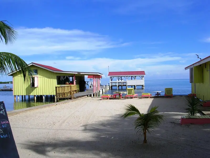 Bâtiments colorés sur pilotis au-dessus de l'eau turquoise, avec une plage de sable clair.