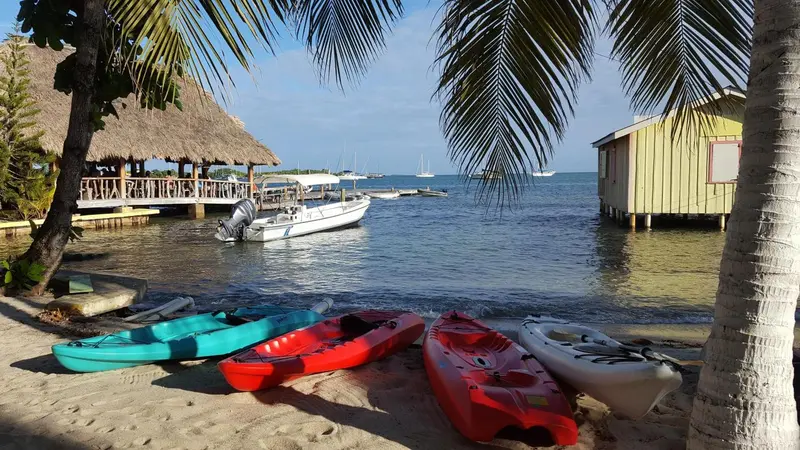 Plage de sable avec des kayaks au premier plan et des bâtiments sur pilotis en arrière-plan.