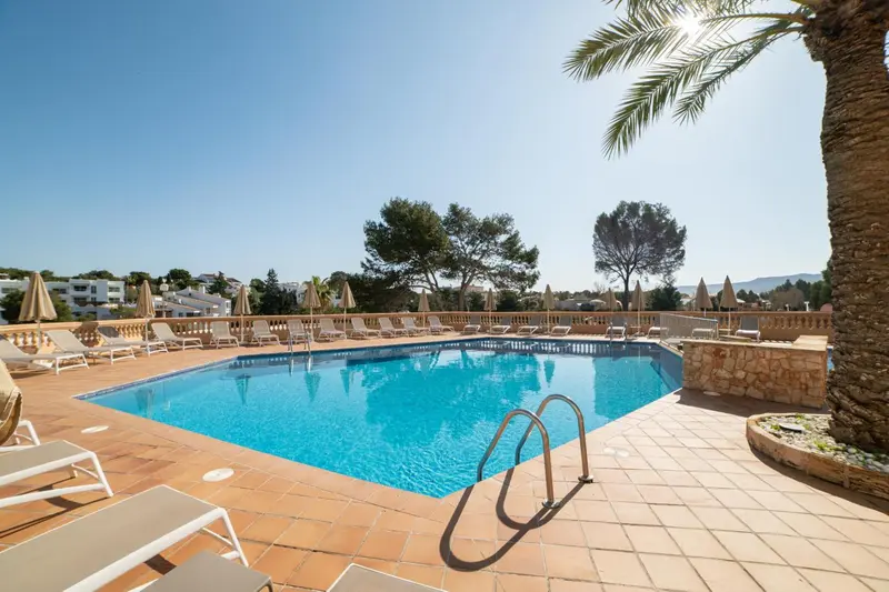 Une piscine rectangulaire bordée de transats sous le soleil.