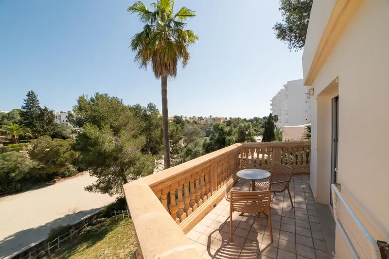 Une terrasse ensoleillée offre une vue sur la végétation et les bâtiments environnants.
