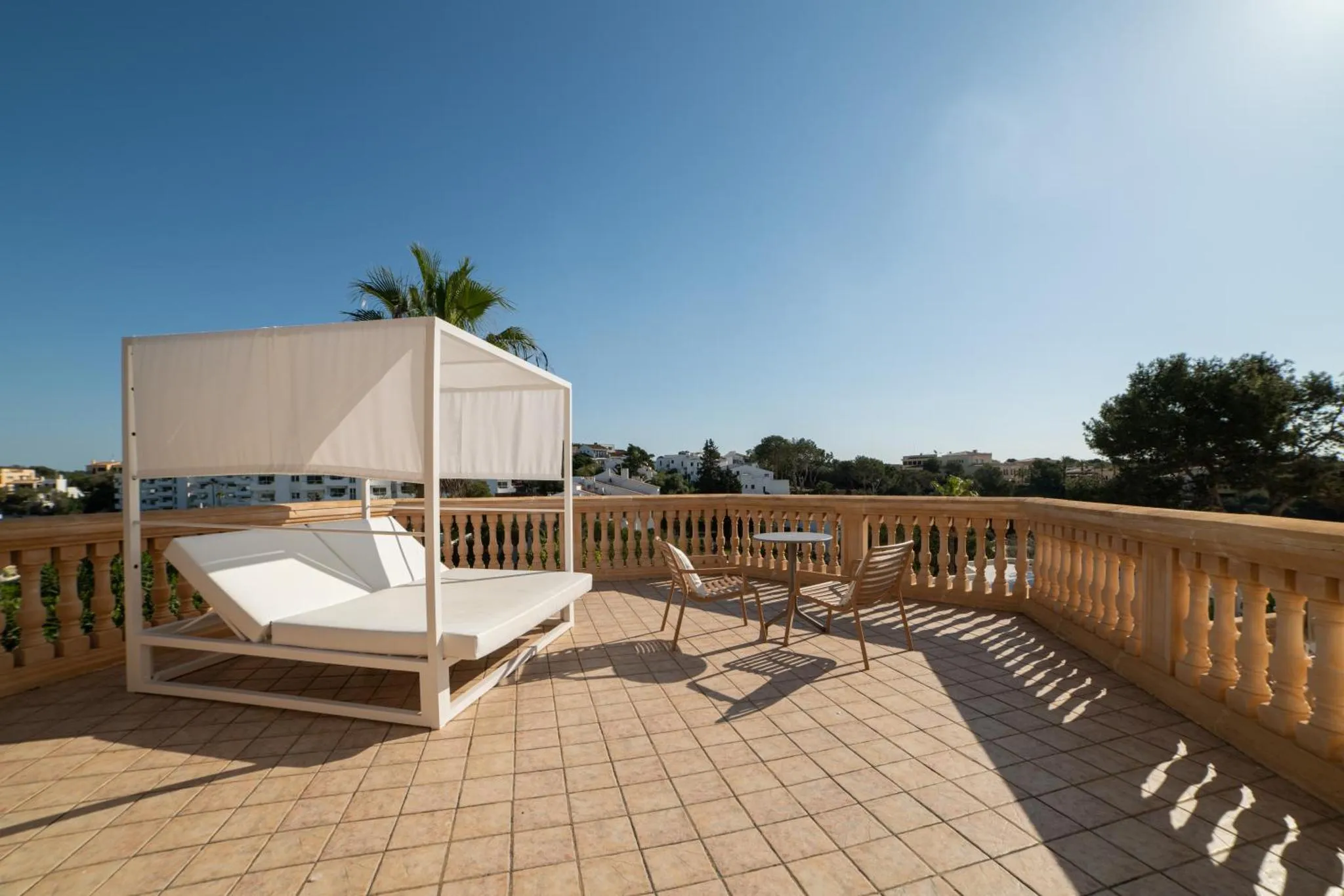 Transats blancs sur une terrasse ensoleillée avec vue sur la mer et la végétation.