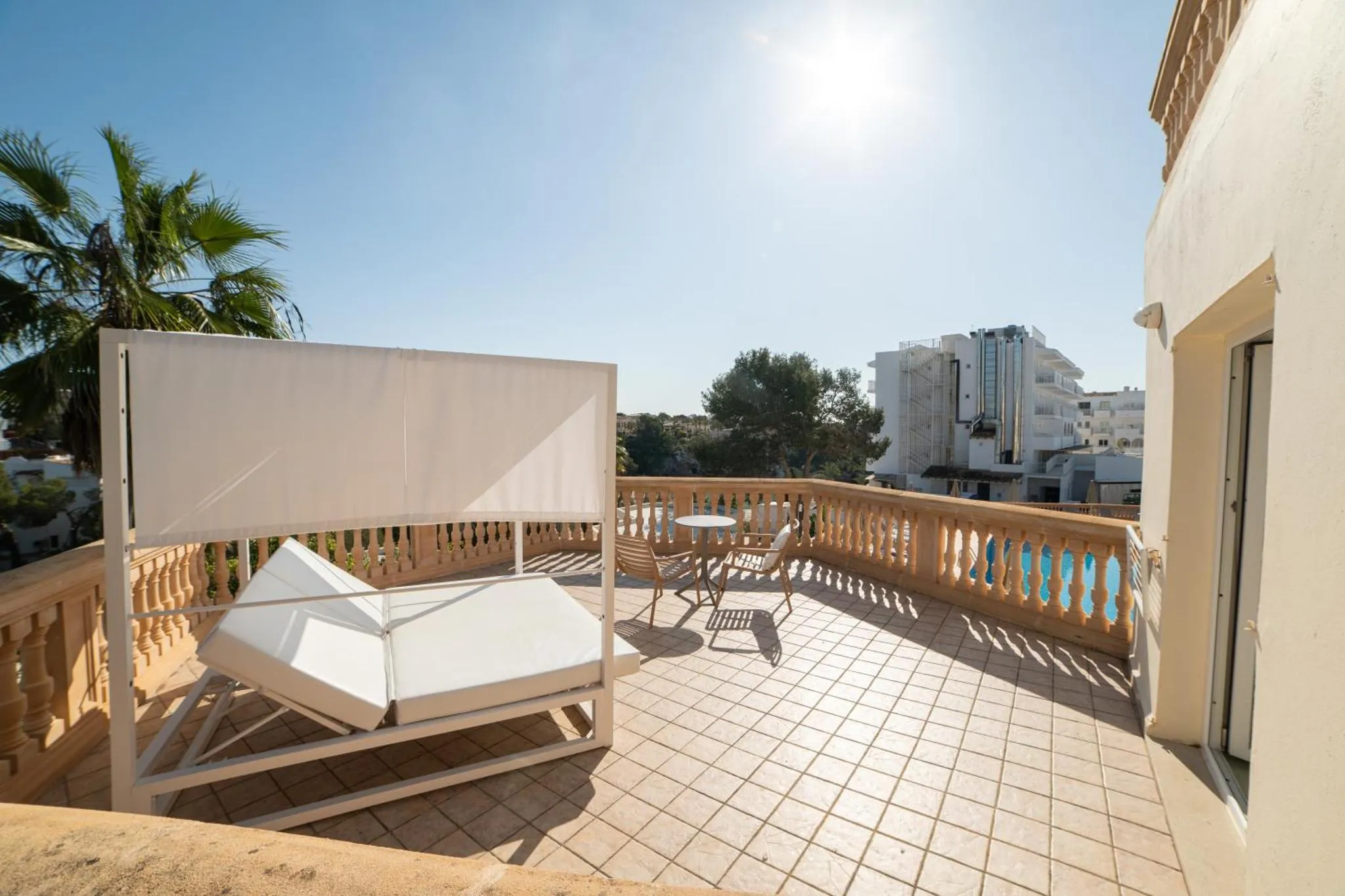Terrasse carrelée avec transats et table basse, vue sur la mer et les bâtiments environnants.