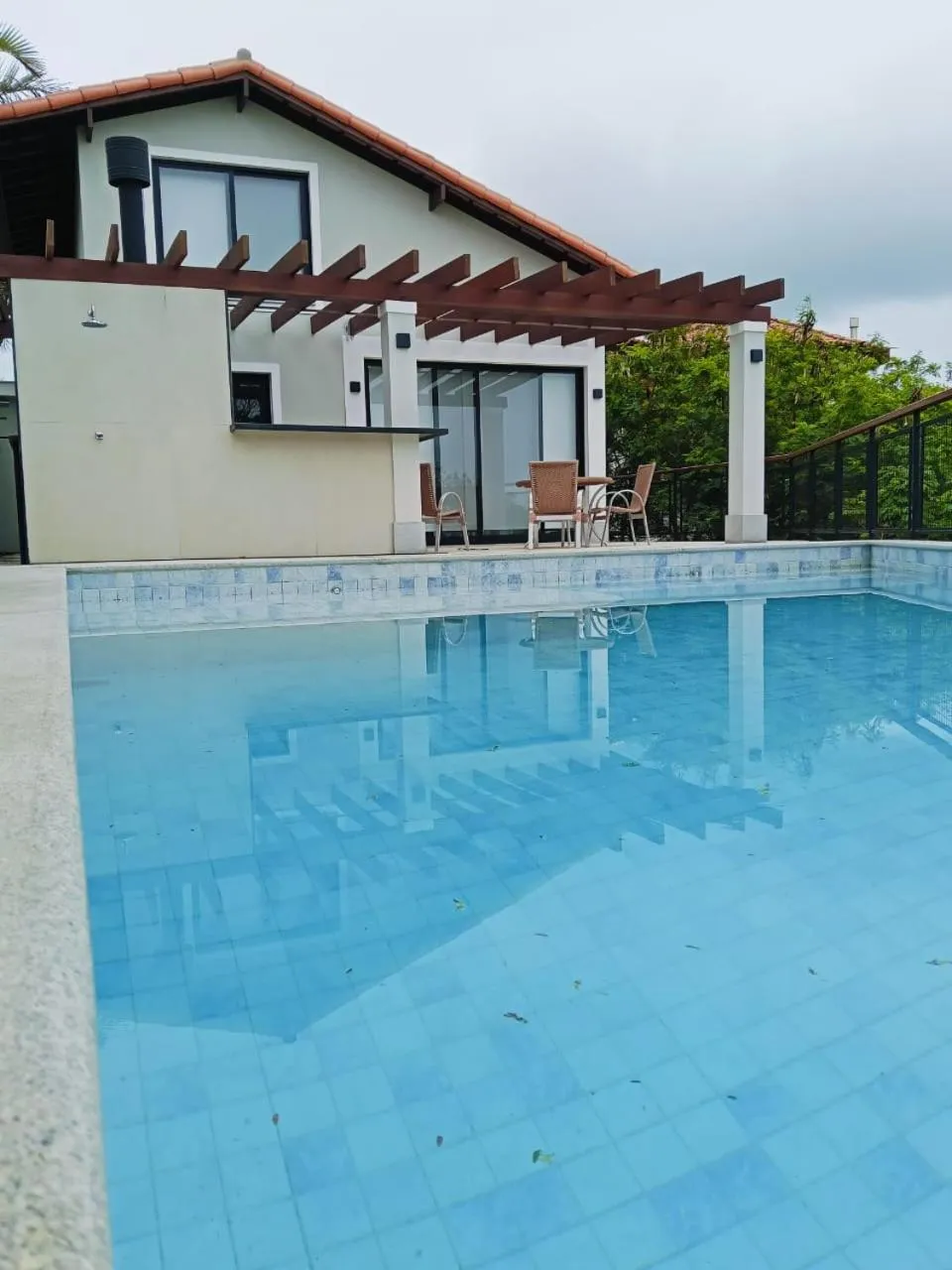 Une piscine rectangulaire turquoise reflète un bâtiment blanc avec une terrasse ombragée.