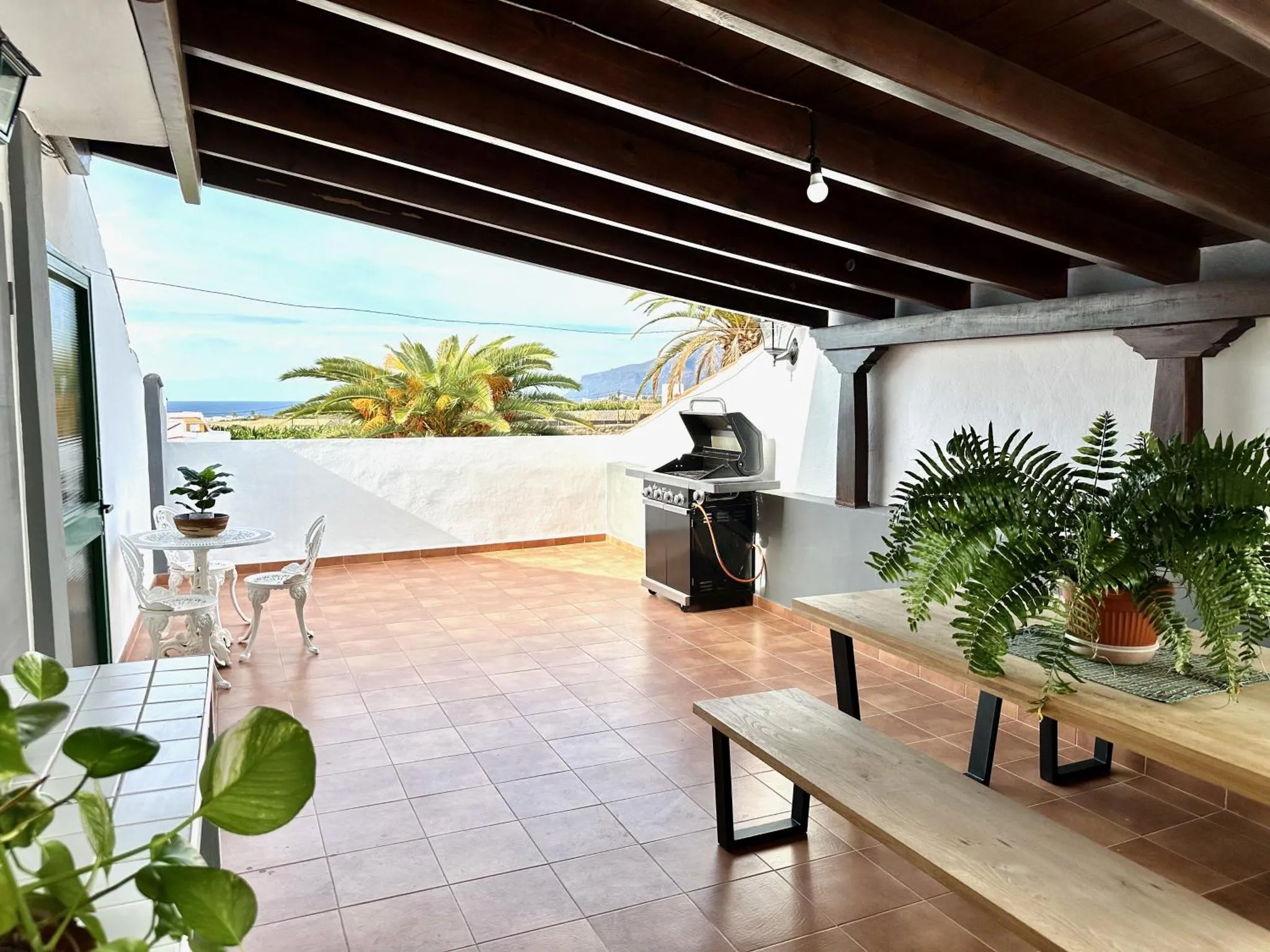 Terrasse carrelée avec mobilier de jardin et barbecue face à la mer.