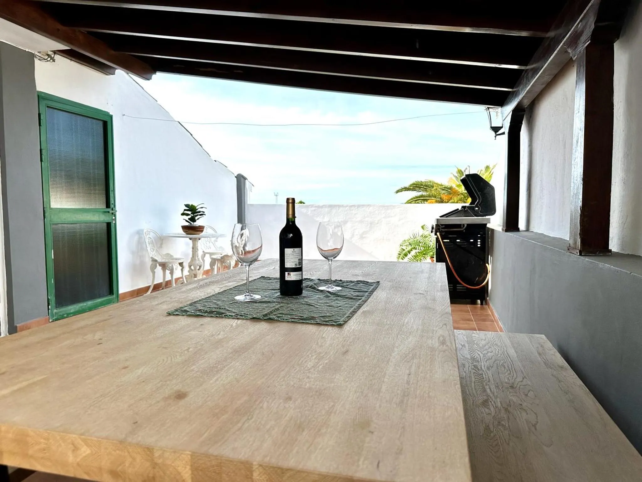 Une table en bois est mise en scène sur une terrasse avec des verres et une bouteille de vin.