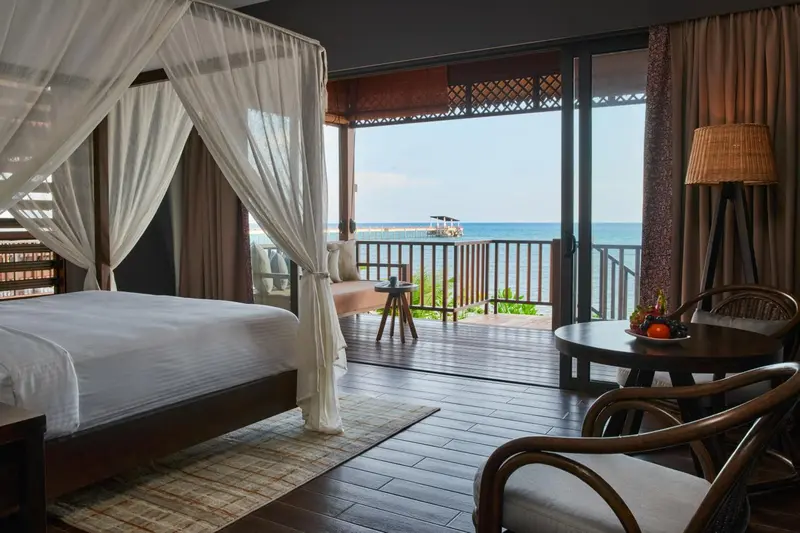 Une chambre lumineuse avec un grand lit à baldaquin donnant sur une terrasse et la mer.