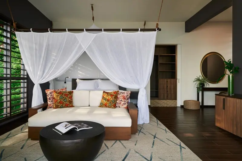 Un lit à baldaquin blanc se trouve dans une chambre décorée de coussins colorés et d'un tapis.