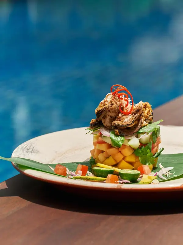 Assiette de salade de fruits de mer colorée, présentée sur une table en bois près d'une piscine.
