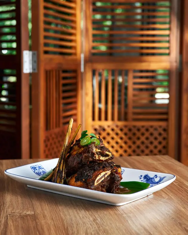 Assiette de viande grillée décorée de citron vert et de brochettes, présentée sur une table en bois.