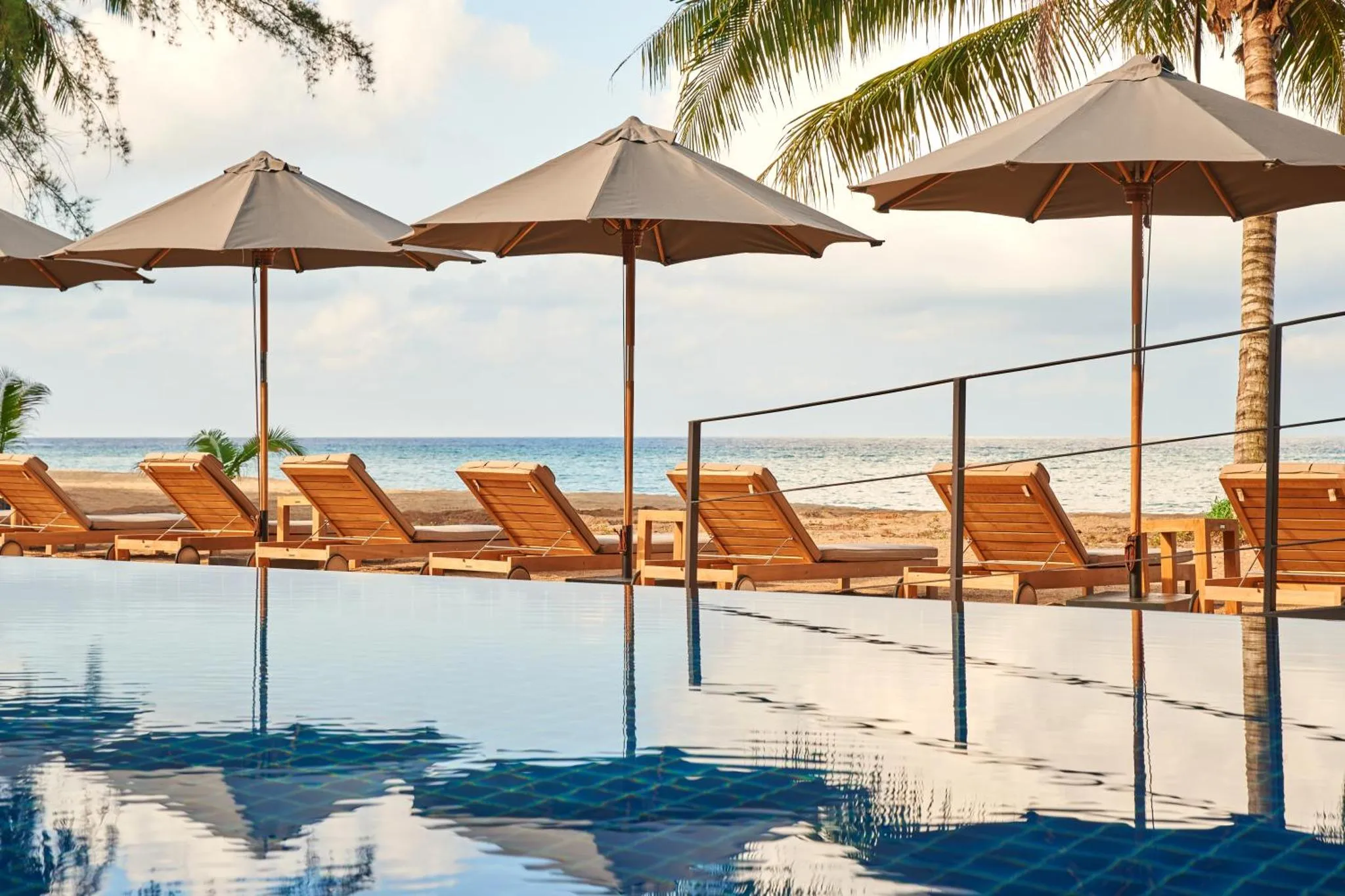 Transats et parasols bordent une piscine à débordement avec vue sur la mer.