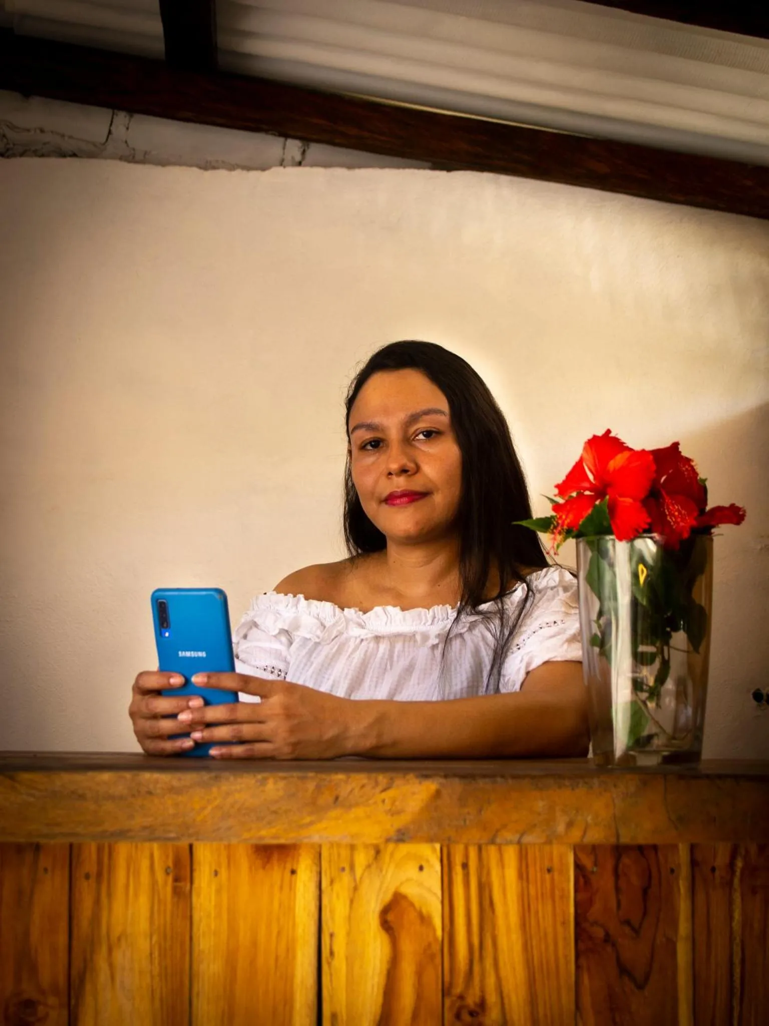 Une femme souriante utilise un smartphone devant un vase de fleurs.