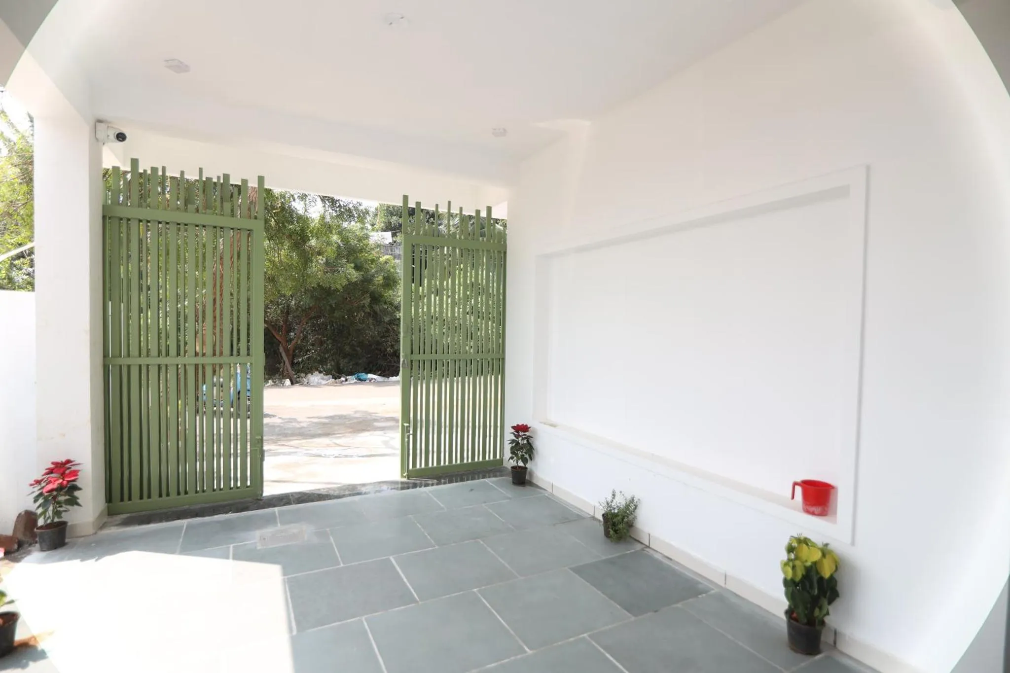 Entree d'une cour avec un portail ouvert et des plantes en pots.