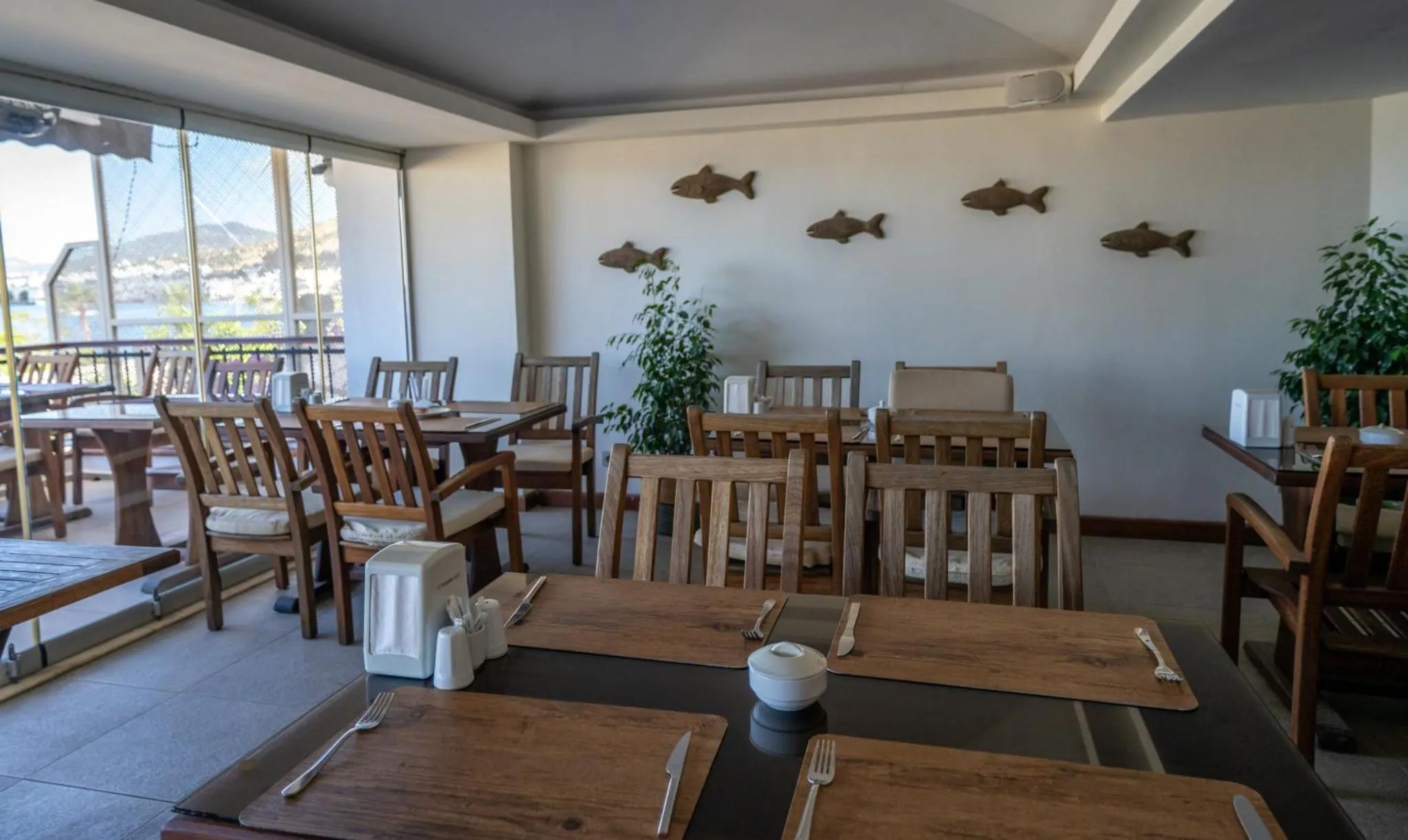 Une salle lumineuse avec des tables et des chaises en bois, donnant sur une vue mer.