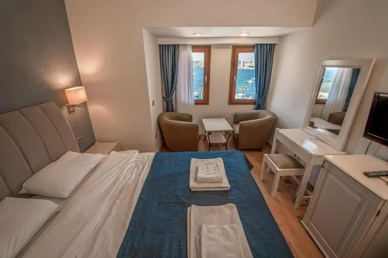 Chambre lumineuse avec un lit et un coin salon près de la fenêtre.