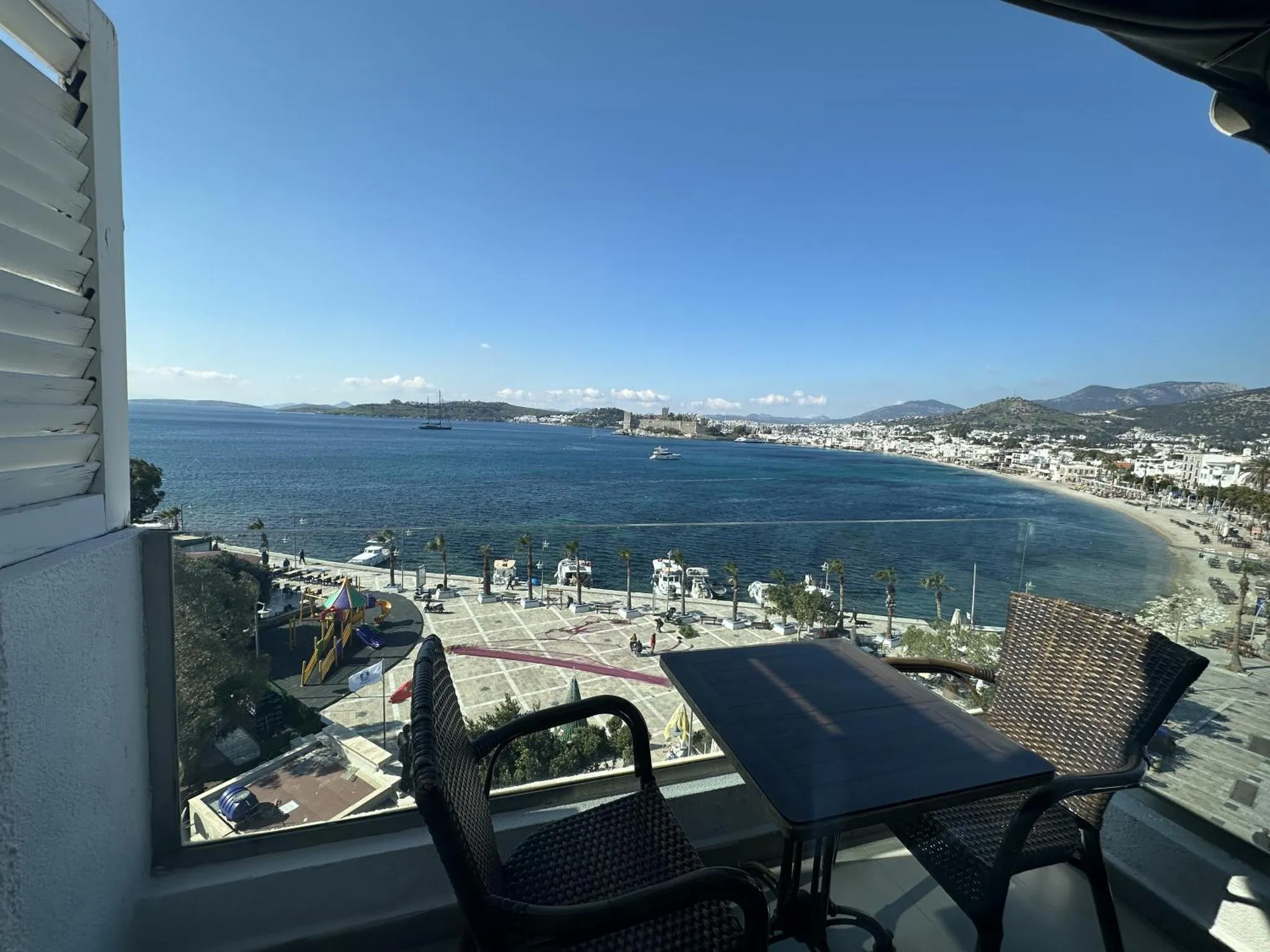 Vue d'une terrasse avec table et chaises donnant sur la mer et une plage.