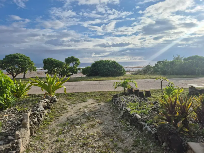 Un jardin tropical s'ouvre sur une plage de sable clair sous un ciel nuageux.