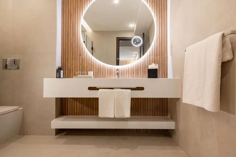 Une salle de bain moderne avec un grand miroir rond et un meuble-lavabo blanc.