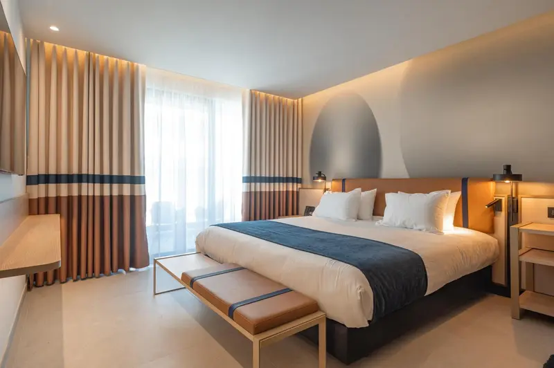 Une chambre lumineuse avec un grand lit et des rideaux beiges.