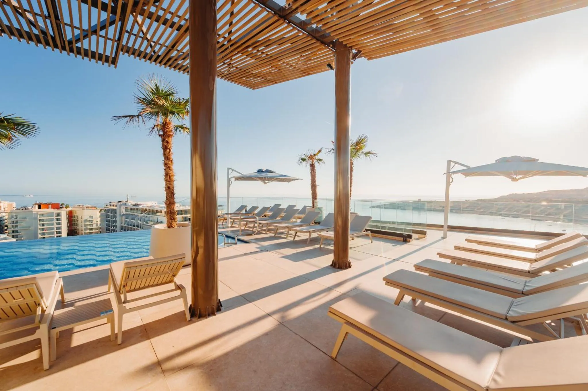 Terrasse avec transats et piscine à débordement offrant une vue sur la mer.