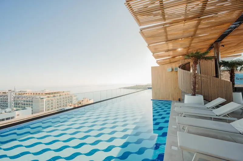 Piscine à débordement avec transats et vue sur la mer.