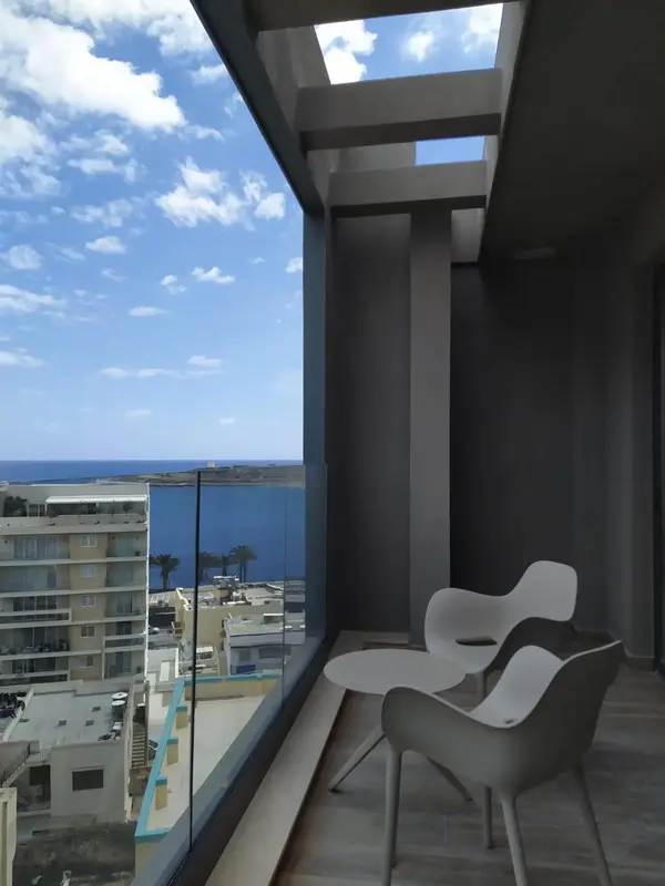 Vue sur la mer depuis un balcon aménagé avec des fauteuils blancs.